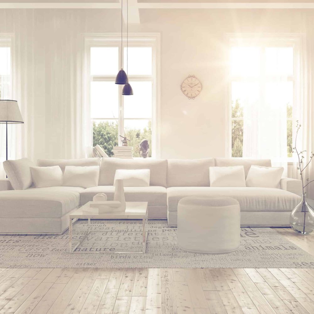 Modern spacious lounge or living room interior with monochromatic white furniture and decor below three tall bright windows with a dark bookcase accent in the corner