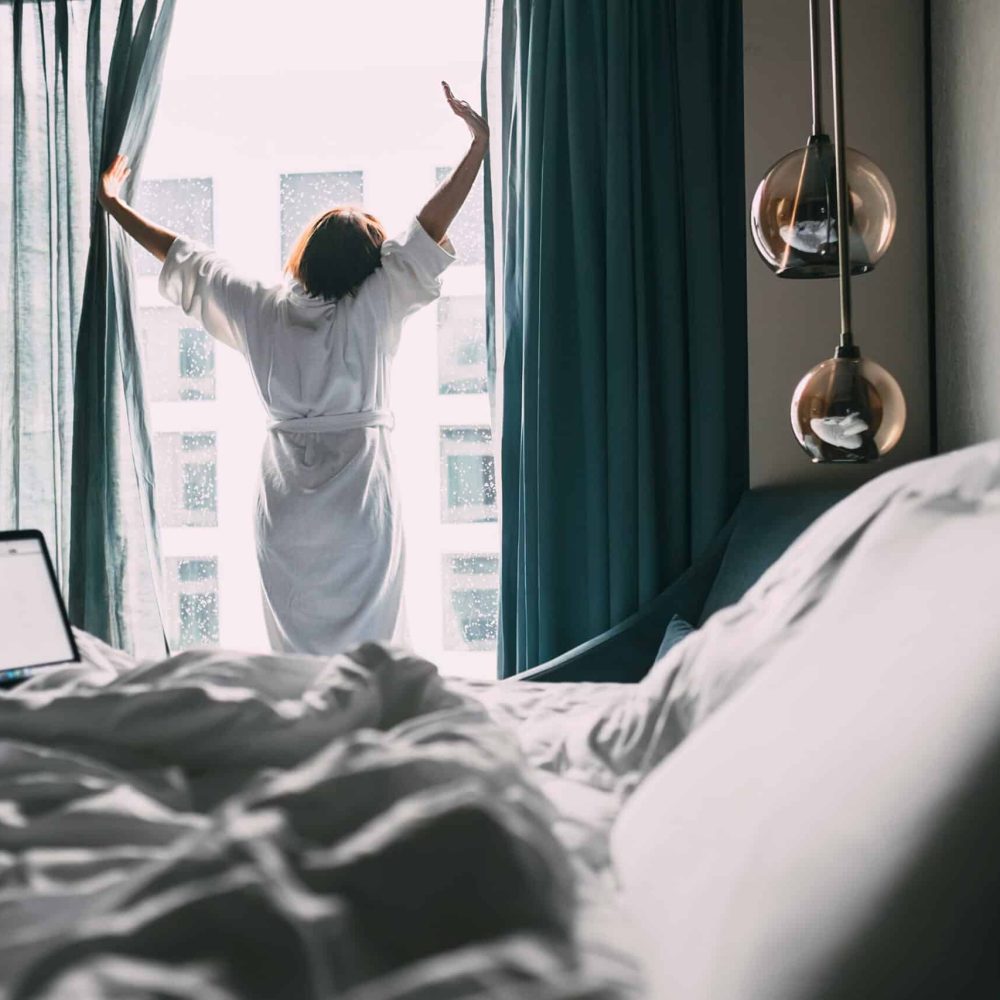 Woman stands near the window in hotel room at morning time